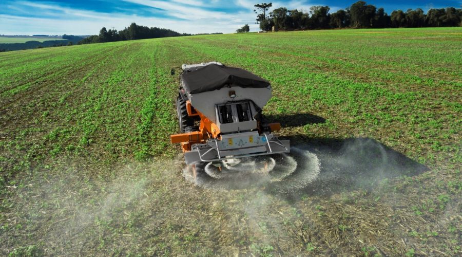 Maquinário agrícola fazendo aplicação de fertilizantes numa lavoura.