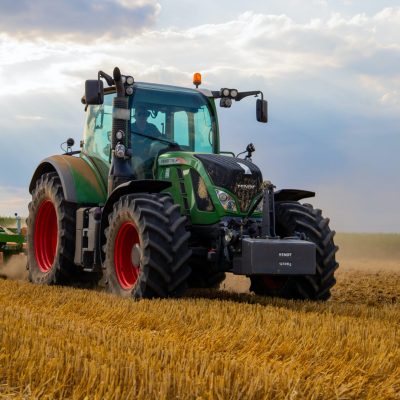 Um trator verde desbravando um vasto campo de plantação.