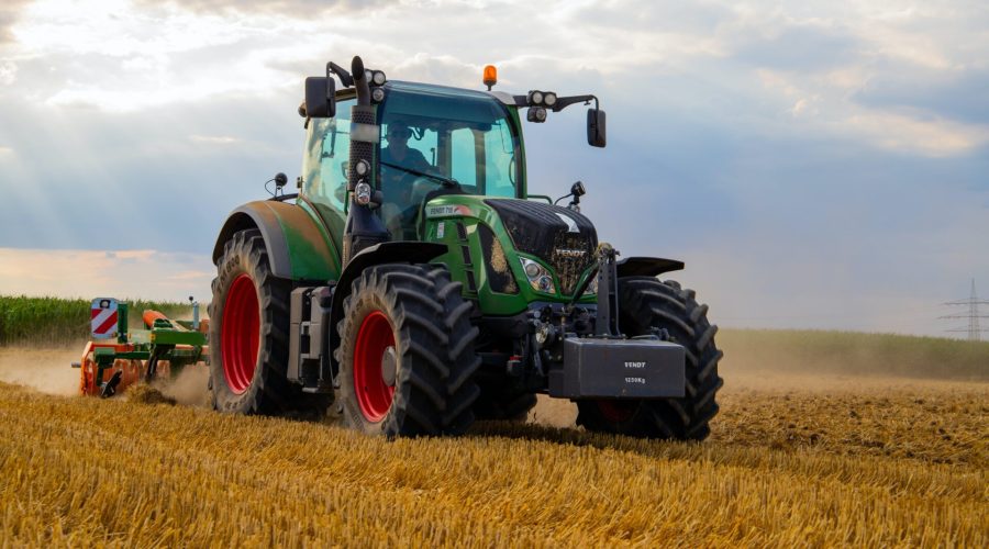 Um trator verde desbravando um vasto campo de plantação.